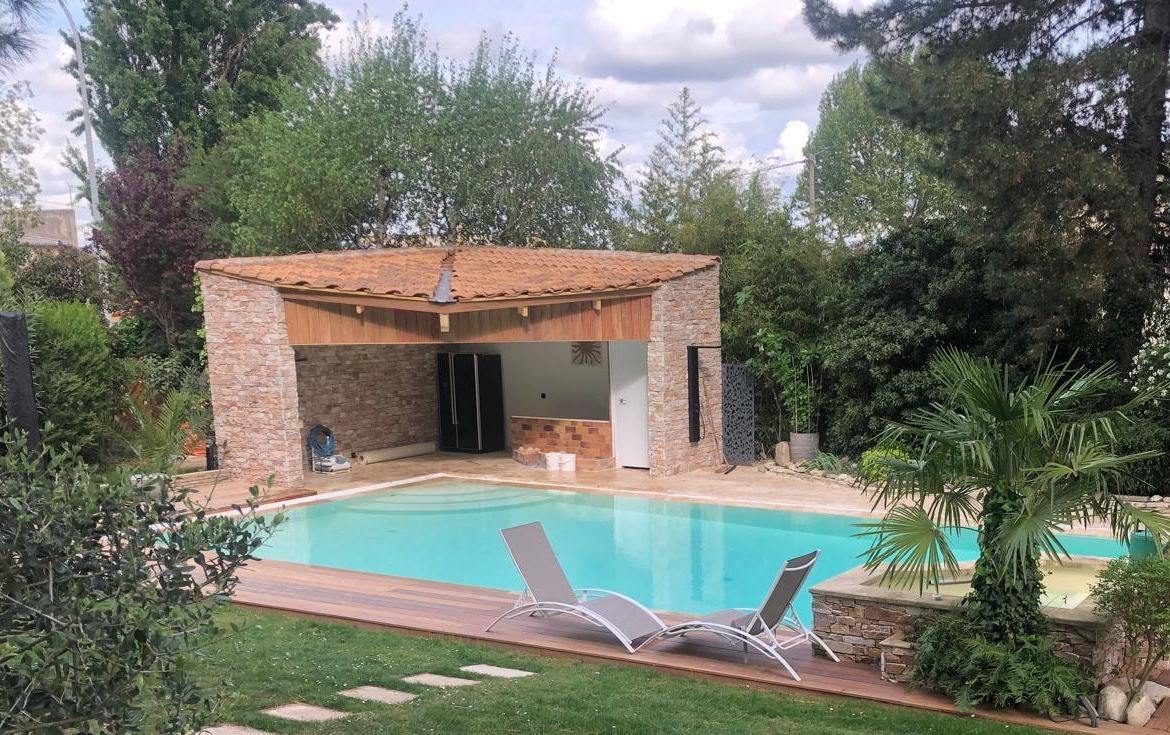 Pool house en pierre et bois avec terrasse en lames de bois au bord d'une piscine — Les Menuiseries de Malo